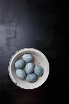 Easter eggs painted blue in white bowl on black wooden background. Top view Stock Photos