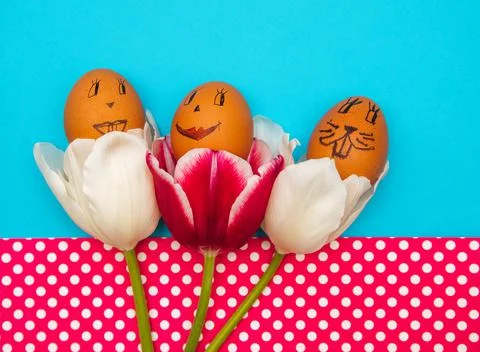 Easter eggs with painted faces and smiles in pink tulips on a blue background Stock Photos