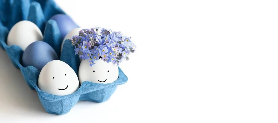 Easter eggs with painted faces and flowers in a blue cardboard box on a white Stock Photos