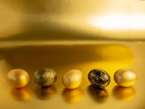 Easter eggs, painted in gold and black, lie in a row on a Golden iridescent.. Stock Photos