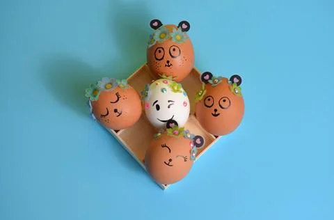 Easter eggs with painted muzzles in a box on a blue background. Easter. Stock Photos