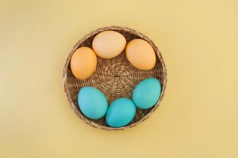 Easter eggs painted in yellow and blue pastel colors in a basket on a yellow Stock Photos