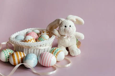 Easter eggs in pastel colors with a pattern and a white toy rabbit in a basket Stock Photos