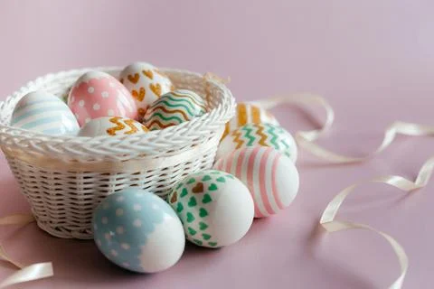 Easter eggs in pastel colors with a pattern in white basket on pink background. Stock Photos