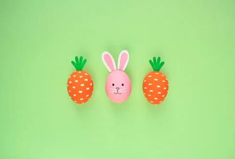 Easter eggs pattern made with painted carrots and bunny on green background Stock Photos