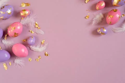 Easter eggs, pink and violet, golden foil and feathers on the violet background Stock Photos
