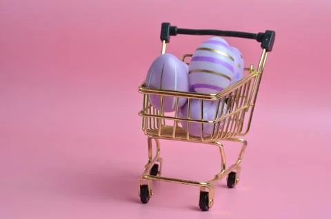 Easter eggs of purple color with patterns. Shopping cart. Pink background. Ea 库存照片