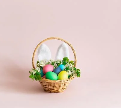Easter eggs with rabbit ears and flowers in a basket on a pink background. Ea Stock Photos