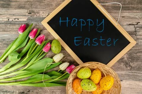 Easter eggs on a table with basket tulips and a blackboard Stock Photos