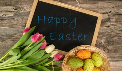 Easter eggs on a table with basket tulips and a blackboard Stock Photos