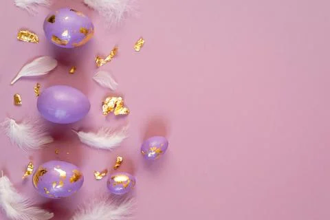 Easter eggs, violet or very peri with golden foil and white feathers on violet Stock Photos