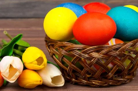 Easter eggs in wicker basket, red and yellow tulips on wooden boards. Stock Photos