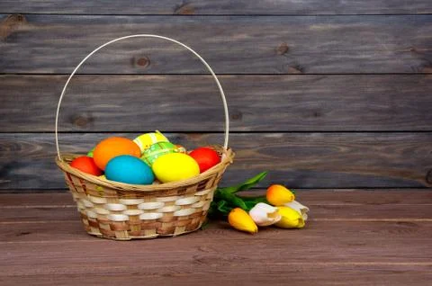 Easter eggs in wicker basket, red and yellow tulips on wooden boards. Stock Photos