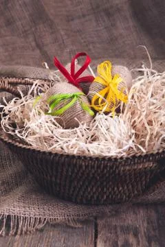 Easter eggs wrapped woolen string in brown basket on rustic wooden background Stock Photos
