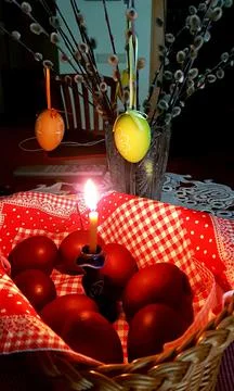 Easter festive composition of a candle and colored chicken eggs in a basket Stock Photos