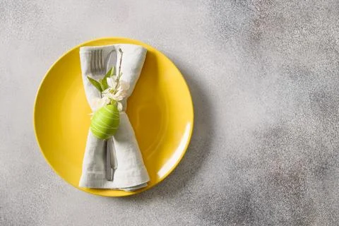 Easter festive table setting with yellow plate, spring flowers and green eggs Stock Photos