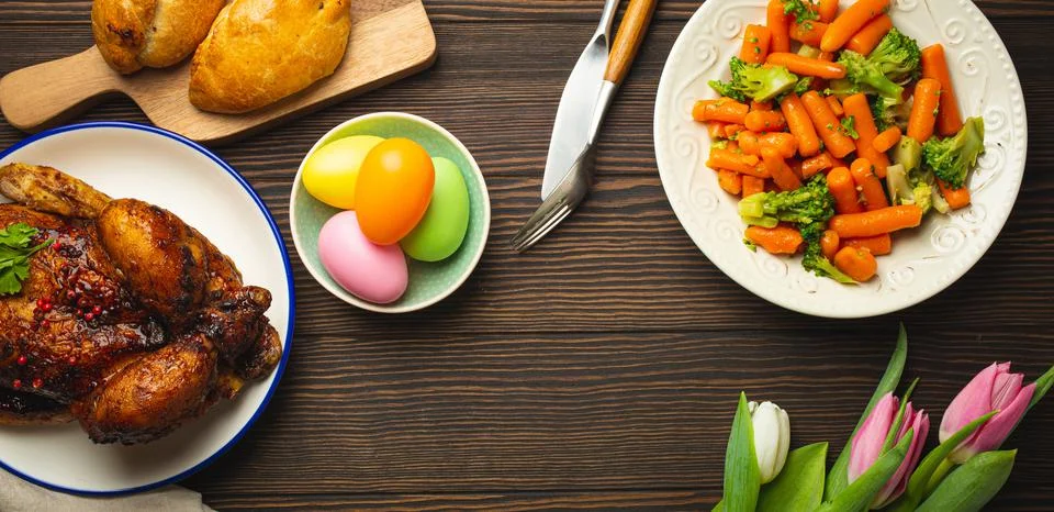 Easter food on dark rustic table: pastel colored eggs, roasted chicken Stock Photos