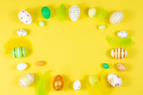 Easter frame with eggs and feathers on a yellow background. Minimal concept Stock Photos