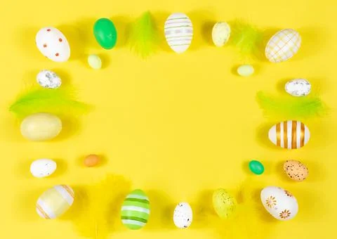 Easter frame with eggs and feathers on a yellow background. Minimal concept Stock Photos