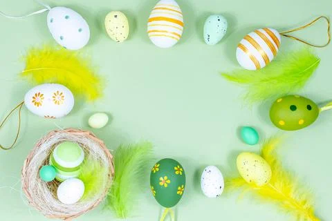 Easter frame with eggs, feathers and a nest on a green background. Minimal Stock Photos