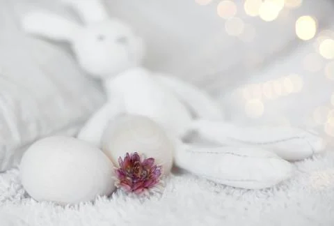 Easter funny white stuffed rabbit toy on a white bed with wooden eggs zero west. Stock Photos
