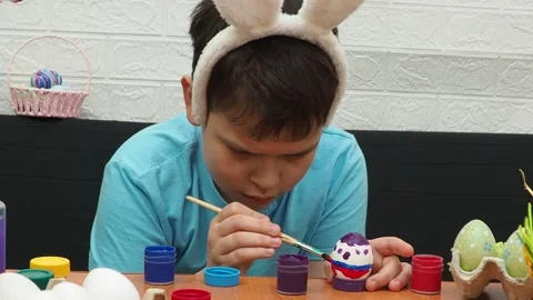 Easter holiday.  bunny ears. A boy  paints an Easter egg. Preparing for Easter 動画素材 173757595