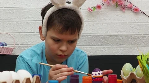 Easter holiday.  bunny ears. A boy  paints an Easter egg. Preparing for Easter 動画素材 173763254