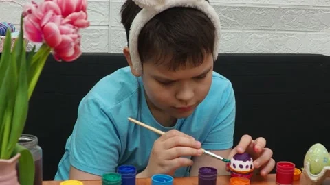 Easter holiday.  bunny ears. A boy  paints an Easter egg. Preparing for Easter 動画素材 173765042