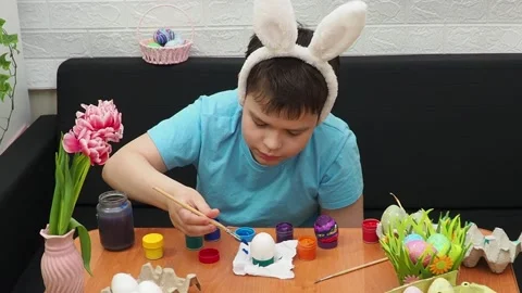 Easter holiday.  bunny ears. A boy  paints an Easter egg. Preparing for Easter 動画素材 173769320
