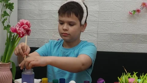 Easter holiday.  bunny ears. A boy  paints an Easter egg. Preparing for Easter 動画素材 173774381