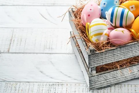 Easter holiday. Colorful Easter eggs in wooden basket on white wooden backg.. Stock Photos