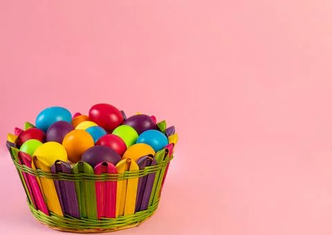 Easter layout. Multi-colored eggs lie in a wicker basket, pink background. Stock Photos