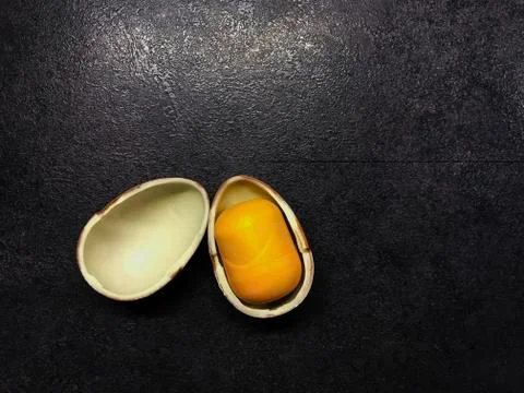 Easter open chocolate kinder egg with a yellow core on a black table Stock Photos