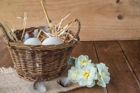 Easter or spring concept: hen eggs in wicker basket with straw and bouquet of Stock Photos