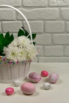 Easter pink and multi-colored eggs near a basket with white flowers on a wooden Stock Photos