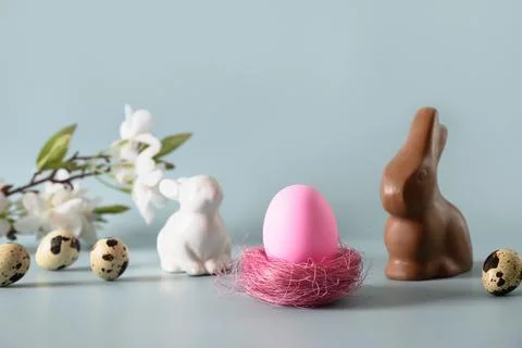 Easter pink egg and chocolate bunny in spring composition on blue. Stock Photos