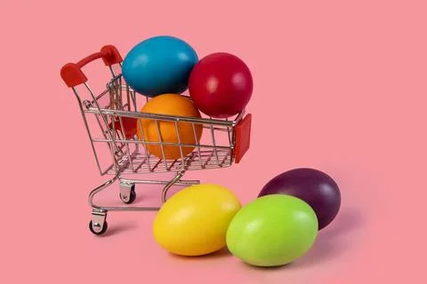 Easter postcard .Shopping cart with multi-colored eggs on a pink background . Stock Photos