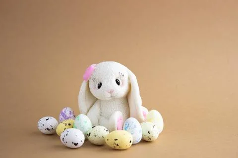 An Easter rabbit made of white chocolate sits among colored eggs on a beige b Stock Photos