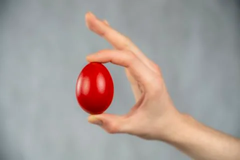 Easter red egg sandwiched between fingers on white abstract background. Foto stock