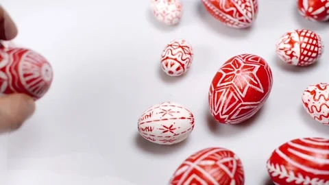 Easter red eggs with folk pattern lay around white. Man hand rotate one egg. Stock Footage 127888442