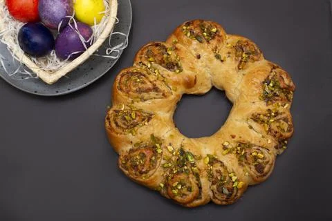 Easter roll with nuts and colored eggs in heart shaped basket. Brown background Stock Photos