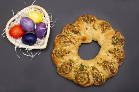 Easter roll with nuts and colored eggs in heart shaped basket. Brown background Stock Photos