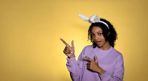 Easter studio shot with cute young woman in easter bunny ears pointing at empty Stock Photos