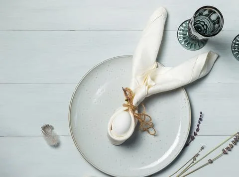 Easter table. An egg wrapped in a rabbit-ear napkin on a gray plate. on a light Stock Photos