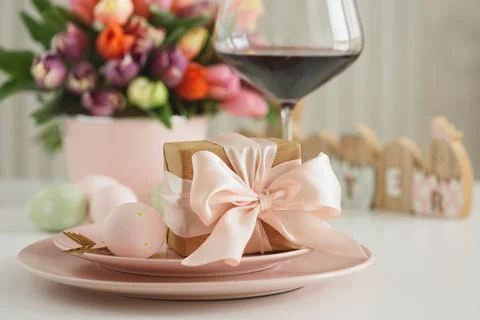 Easter Table Setting with Gift Box, Decorated Eggs, Wine Glass and Tulips. .. Foto stock