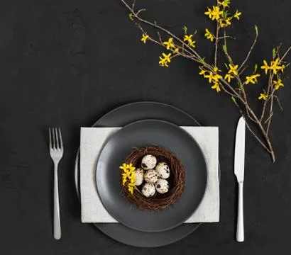 Easter table setting with a nest of quail eggs , a napkin and yellow flowers  Stock Photos