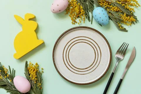 Easter table setting. Plate with easter eggs and mimosa on a pastel green b.. Stock Photos