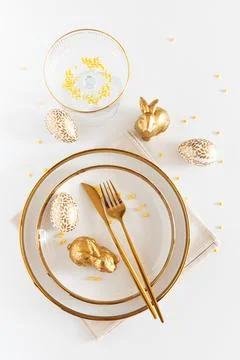 Easter Table Setting with Plates and Golden Decor on White Table Foto stock