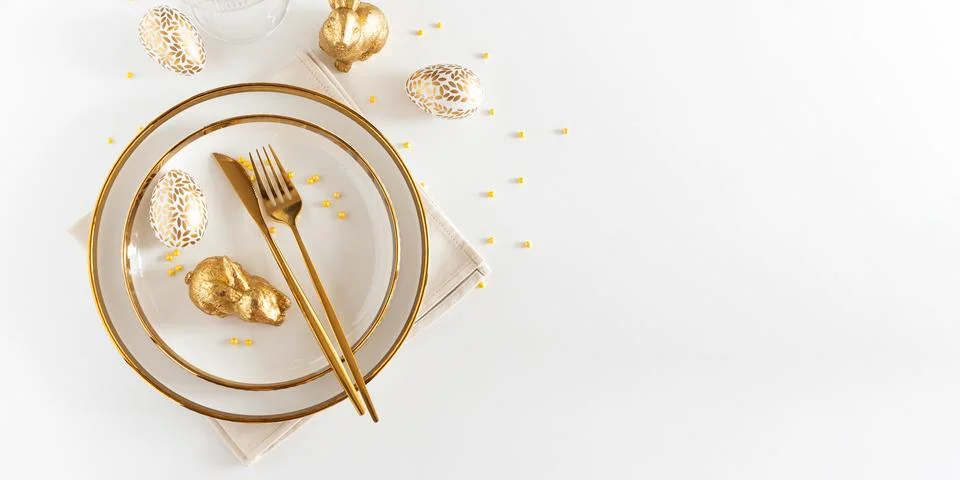 Easter Table Setting with Plates and Golden Decor on White Table Foto stock