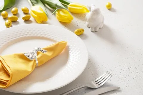Easter table setting with yellow tulips, white plate, eggs and bunny. Stock Photos
